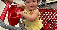 Mia is registered to the contest to win money with this photo: baby, child, shopping_cart, target, store, retail, grocery, person, toddler, yellow_dress, blue_bow, hand, floor, shelves, products, cosmetics, smile, happy, indoor, shopping
