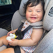 Mia is registered to the contest to win money with this photo: baby, child, car_seat, toy, unicorn, smiling, happy, curly_hair, striped_clothing, safety_harness, infant, cute, indoors, seatbelt, car_interior, portrait, person, baby_toy, plush_toy, candid