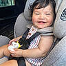 baby, child, car_seat, toy, unicorn, smiling, happy, curly_hair, striped_clothing, safety_harness, infant, cute, indoors, seatbelt, car_interior, portrait, person, baby_toy, plush_toy, candid