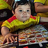 toddler, child, yellow_jersey, bow, menu, restaurant, table, food_photos, people, indoor, curious, seated, family, casual, portrait, hand, face, hair, clothing, group