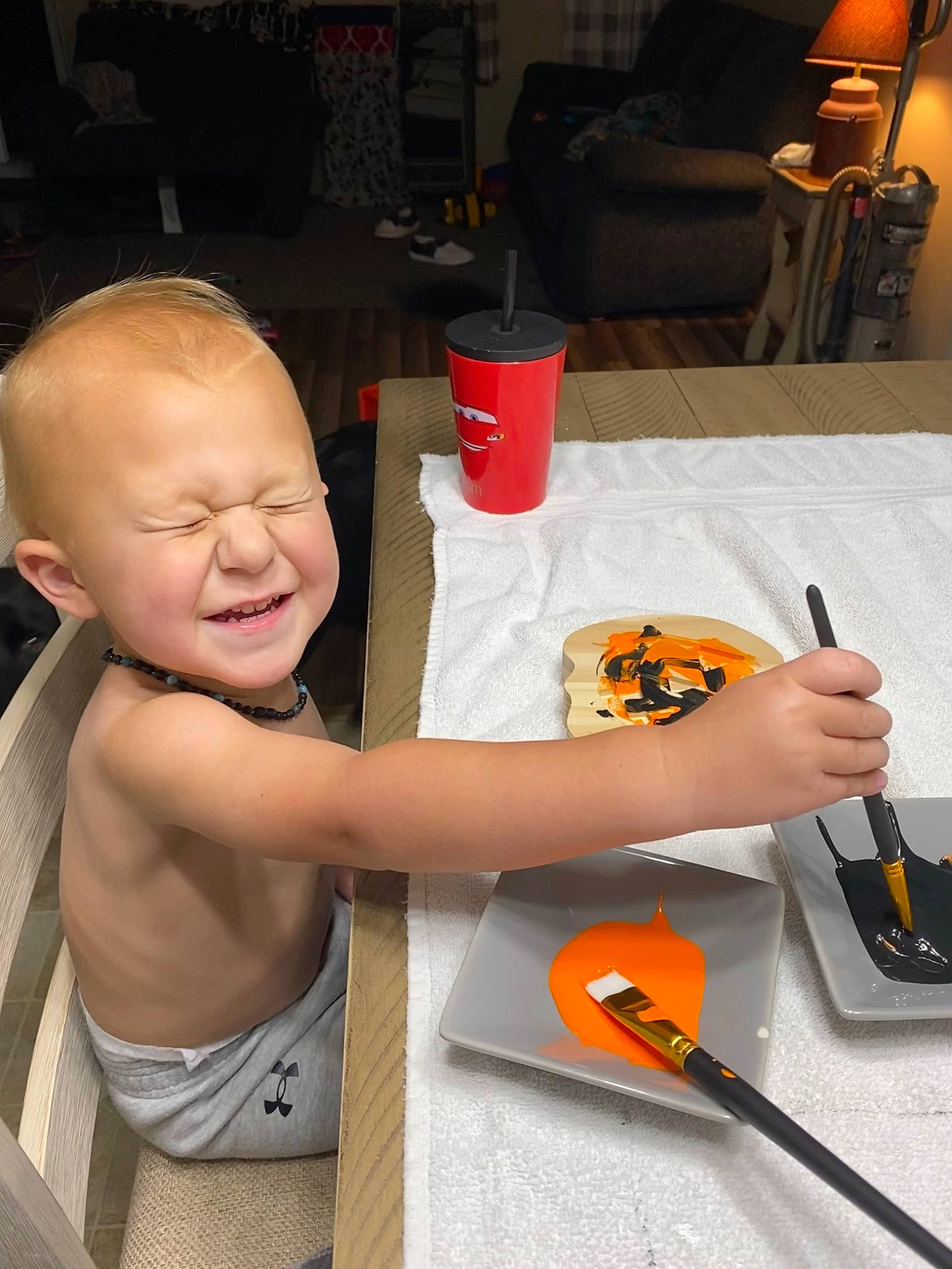 Ryker is registered to the contest to win money with this photo: baby, chair, child, cooking, finger, furniture, hand, joy, kitchen_utensil, office_supplies, orange, pen, person, plate, smile, t_shirt, table, tableware, toddler, tool