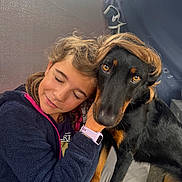 Trann a rejoint le concours — aidez-le/la à gagner de superbes lots ! child, dog, hug, affection, indoor, black_dog, brown_markings, hair, smile, closed_eyes, watching, friendship, cute, pet, furry, portrait, cuddle, jacket, watch, floor