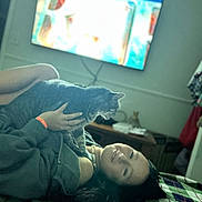 Fiona Flor Cookshot joined the competition — help win amazing prizes! person, cat, tabby_cat, pet, blanket, bed, television, tv, indoor, hand, face, sweater, wristband, necklace, cozy, living_room, furniture, lying_down, whiskers, portrait