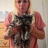 animal, blonde_hair, casual_clothing, cute, domestic, door, dresser, elderly, face, furniture, gray_cat, hands, holding, indoor, kitten, pets, pink_shirt, tabby_cat, woman