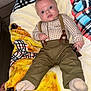 baby, infant, suspenders, pants, socks, blanket, plaid, pattern, blue_eyes, face, hand, lying_down, indoor, cute, young_child, clothing, furniture, wood_floor, expression, portrait