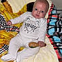 Caleb is registered to the contest to win money with this photo: baby, infant, onesie, blanket, fuzzy, colorful, child, indoor, cute, person, holding, wooden_paddle, smiling, face, head, footed_pajamas, plush, comfort, relaxing, portrait