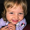 child, toddler, portrait, smiling, happy, face, eyes, teeth, hair, hands, pajamas, purple_clothing, sitting, indoors, sofa, couch, closeup, flash_photography, playful, cheerful