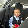 boy, car_interior, casual, child, clothing, daylight, gift, happy, inside, person, portrait, seat, seatbelt, shirt, smile, transportation, tree, vest, window, young