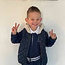 belt, boy, casual_clothing, child, cute, fairy_lights, fashion, gesture, happy, hoodie, indoor, peace_sign, person, playful, portrait, short_hair, smile, standing, vest, white_wall