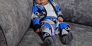 Rayyan is registered to the contest to win money with this photo: baby, child, couch, furniture, indoor, person, clothing, patterned_outfit, sitting, wide_eyes, expression, home, young, cute, infant, socks, wall, texture, seat, casual