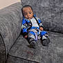 baby, child, couch, furniture, indoor, person, clothing, patterned_outfit, sitting, wide_eyes, expression, home, young, cute, infant, socks, wall, texture, seat, casual