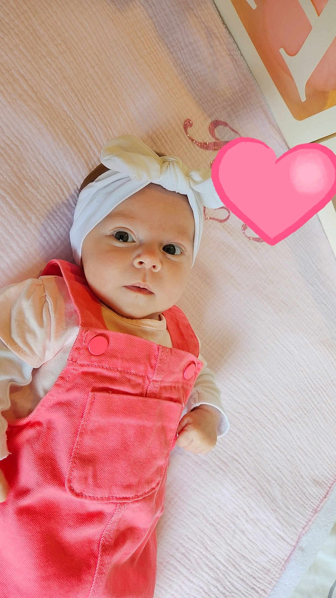 Romy a rejoint le concours — aidez-le/la à gagner de superbes lots ! baby, infant, headband, pink_overall, blanket, lying_down, cute, child, portrait, indoors, soft_texture, white_clothing, adorable, gazing, small_hand, face, head, expression, heart_emoji, cozy