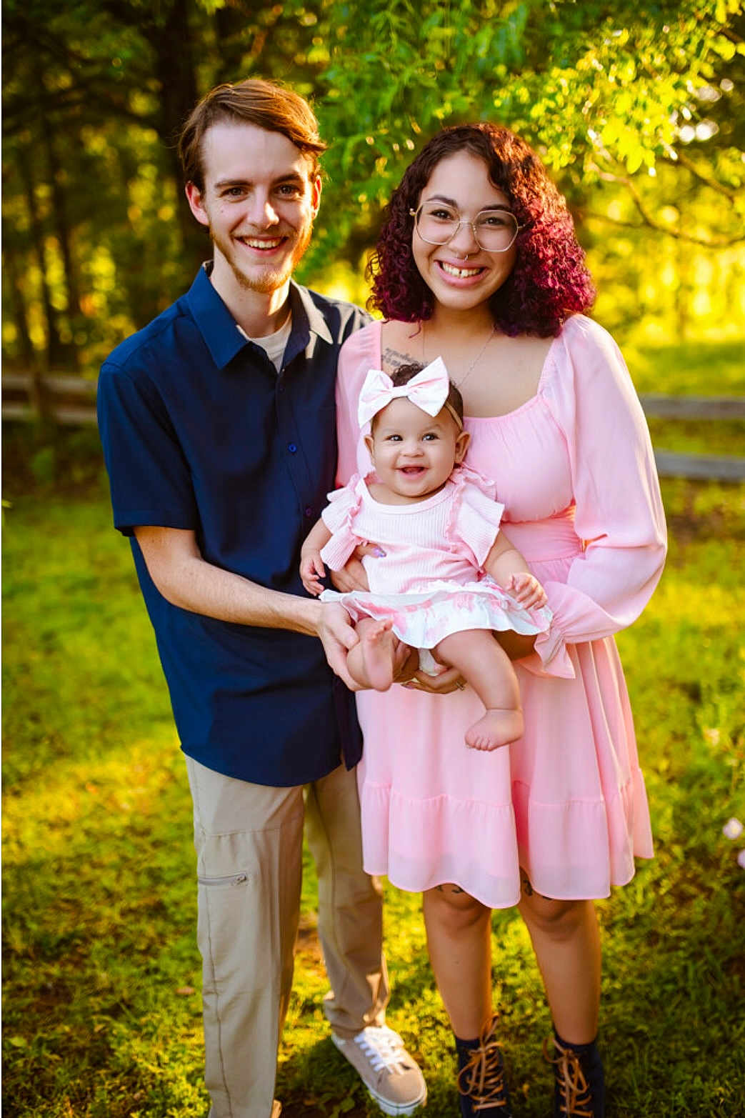 Emersyn is registered to the contest to win money with this photo: family, baby, woman, man, smiling, outdoor, nature, greenery, sunlight, dress, glasses, bow, happy, parent, child, casual_clothing, portrait, holding, grass, daylight
