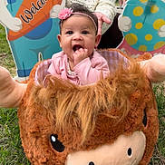 Emersyn joined the competition — help win amazing prizes! baby, child, pink_headband, pink_clothing, plush, stuffed_animal, grass, outdoor, hand, person, cute, smiling, face, head, toy, playful, welcome_sign, colorful, sitting, young_child