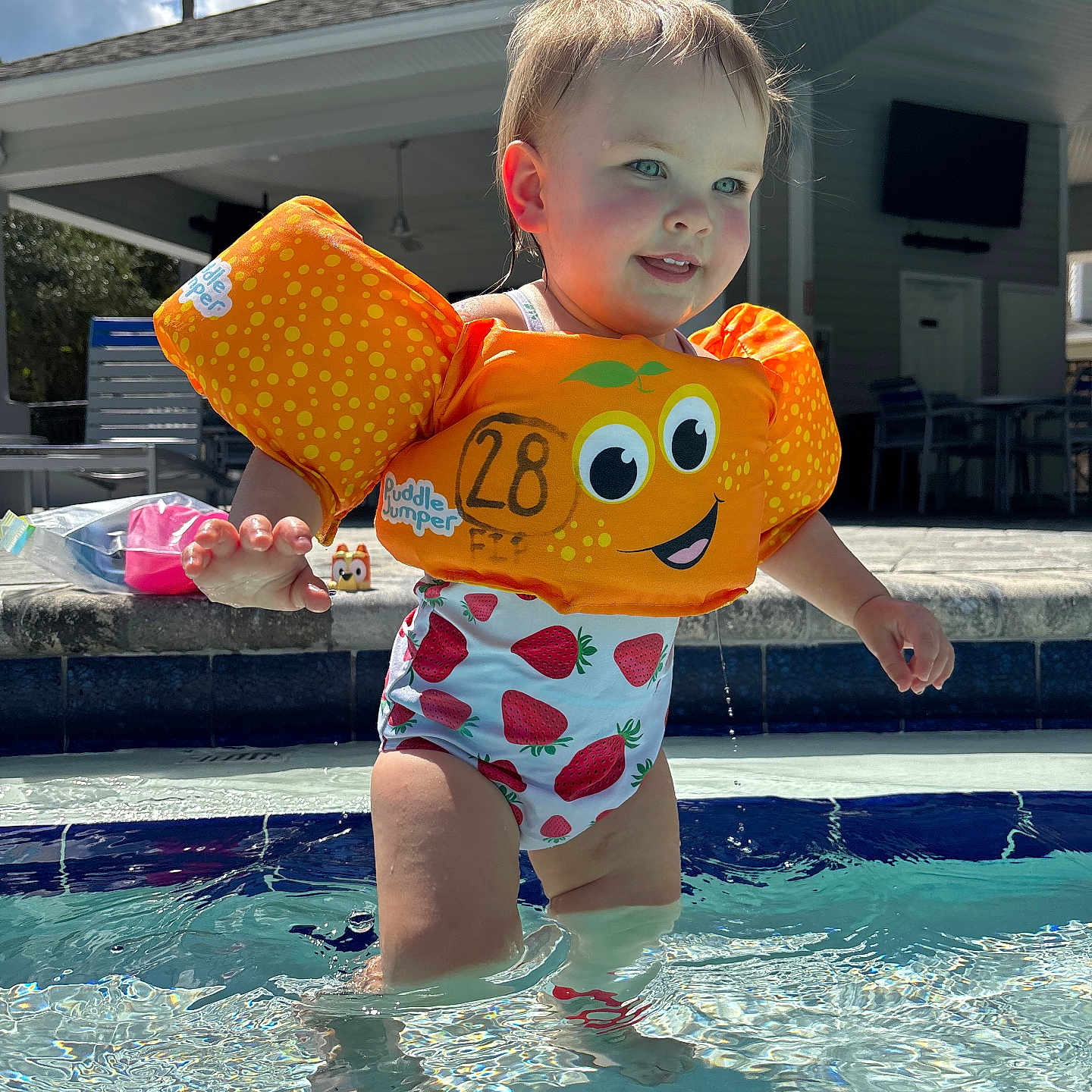 Everlyn joined the competition — help win amazing prizes! blue_eyes, child, clouds, face, floatation_device, happy, orange, outdoor, patio, play, pool, sky, splashing, strawberry_pattern, summer, sunlight, swimsuit, toddler, water, water_droplets