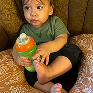 Emilio joined the competition — help win amazing prizes! toddler, child, baby, sippy_cup, cushion, pattern, green, orange, face, expression, curious, sitting, clothing, short_sleeve, indoor, foot, hand, brown, hair, comfort