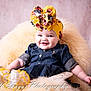 baby, infant, child, headband, floral_bow, denim_dress, wicker_chair, fluffy_throw, smile, portrait, cozy, studio_background, pink_background, rosy_cheeks, sitting, legs, arm, socks, closeup, photography