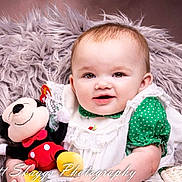 Emma joined the competition — help win amazing prizes! baby, infant, child, portrait, smiling, plush_toy, mickey_mouse, stuffed_animal, fur_blanket, studio_photography, closeup, dress, lace, green_clothing, basket, eyes, rosy_cheeks, soft_texture, watermark, happy