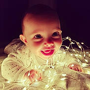 Liv a rejoint le concours — aidez-le/la à gagner de superbes lots ! baby, child, smiling, face, hands, lights, fairy_lights, glowing, blanket, cozy, indoor, cute, happy, infant, portrait, expression, warm, soft_lighting, night, playful