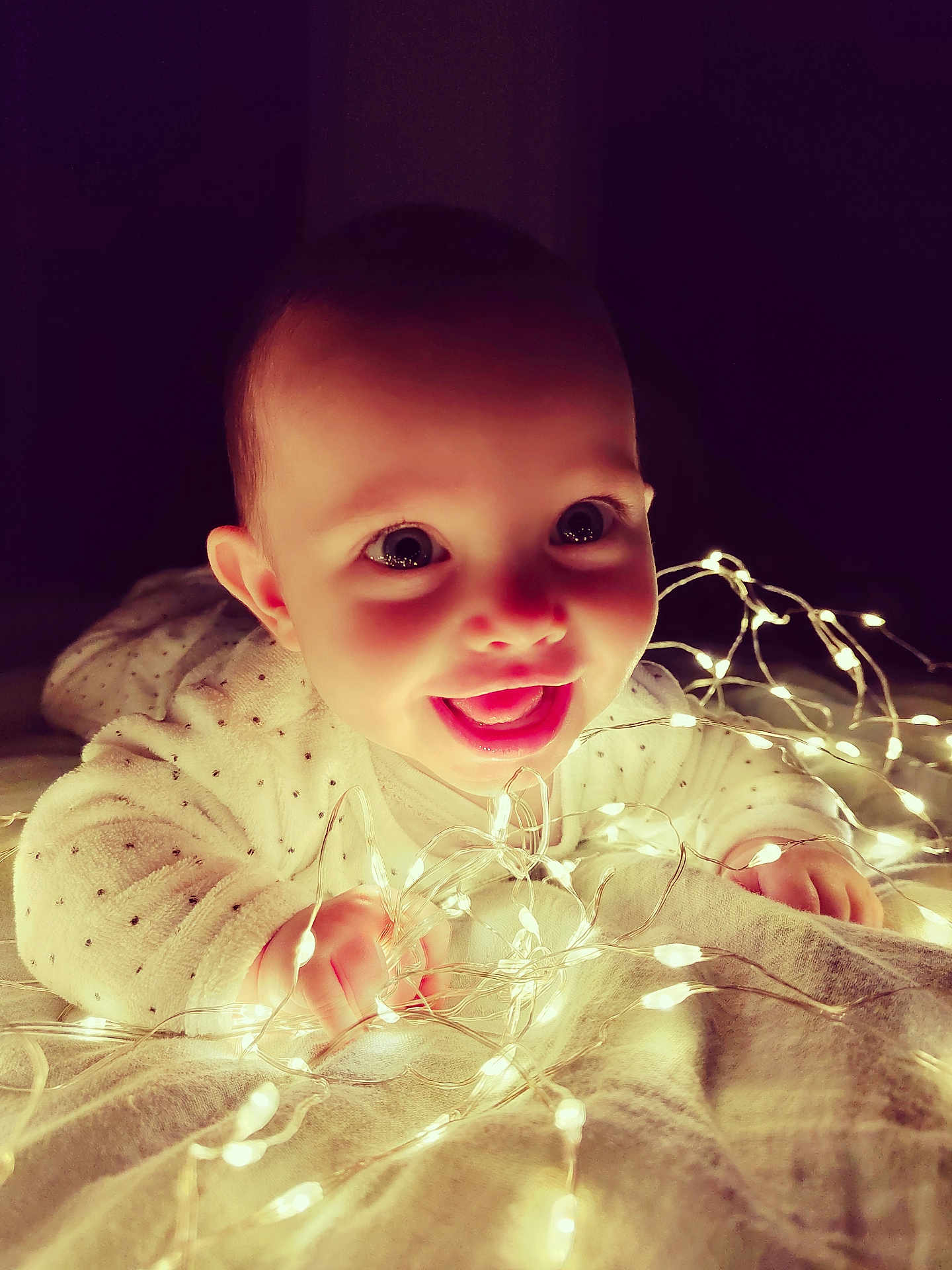 Liv a rejoint le concours — aidez-le/la à gagner de superbes lots ! baby, child, smiling, face, hands, lights, fairy_lights, glowing, blanket, cozy, indoor, cute, happy, infant, portrait, expression, warm, soft_lighting, night, playful