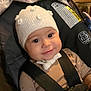 baby, child, infant, car_seat, graco, knitted_hat, white_hat, smile, straps, safety_harness, indoor, blanket, floral_pattern, cute, face, person, seat, comfort, warm_clothing, portrait