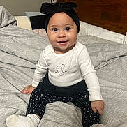 Isabella joined the competition — help win amazing prizes! baby, child, smiling, indoor, bed, blanket, headband, clothing, white_top, black_leggings, socks, cute, happy, portrait, person, infant, young_child, face, eyes, hand