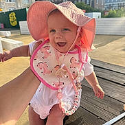 Tiana joined the competition — help win amazing prizes! baby, child, pink_hat, bib, smiling, outdoor, sunlight, building, table, hand, person, cute, happy, summer, pacifier, accessory, clothing, skin, face, daytime
