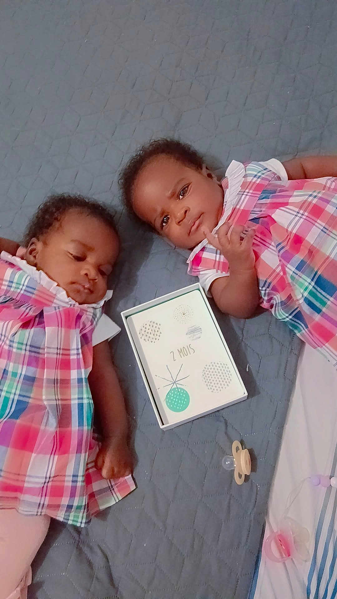 Naomie Et Naelle participe au concours pour gagner de l'argent avec cette photo : baby, infant, toddler, child, plaid_dress, pink, lying_down, blanket, pacifier, toy, card, milestone, cute, face, skin, hair, indoor, sleepy, resting, person