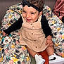 baby, child, smiling, headband, dress, toy, sneakers, sitting, cushion, patterned, indoor, happy, person, clothing, footwear, cute, infant, black, beige, playful