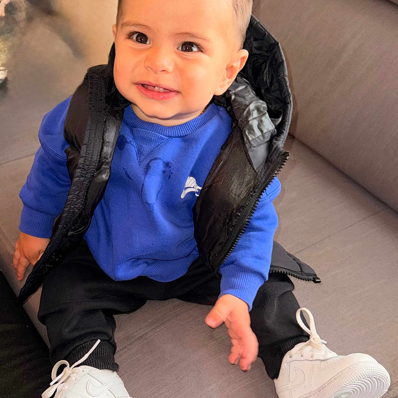 Raphaël a rejoint le concours — aidez-le/la à gagner de superbes lots ! black_pants, black_puffer_vest, blue_sweatshirt, casual_wear, child, comfortable, couch, cute, fashion, footwear, hairstyle, happy, indoor, person, portrait, sitting, smiling, toddler, white_sneakers, young_child