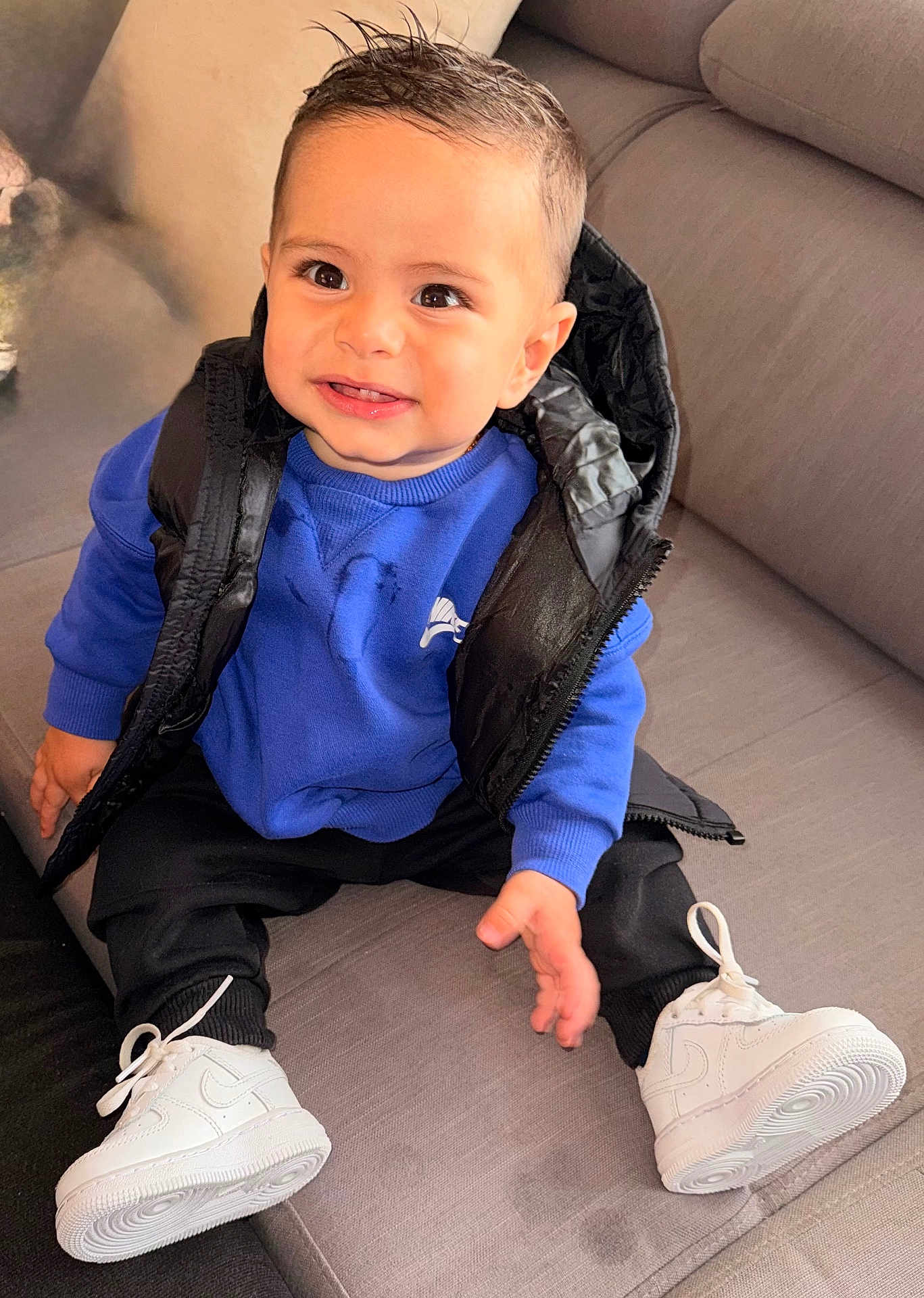 Raphaël a rejoint le concours — aidez-le/la à gagner de superbes lots ! toddler, child, smiling, blue_sweatshirt, black_puffer_vest, black_pants, white_sneakers, couch, indoor, happy, sitting, cute, portrait, fashion, young_child, person, casual_wear, hairstyle, footwear, comfortable