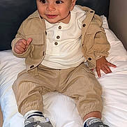 Raphaël a rejoint le concours — aidez-le/la à gagner de superbes lots ! toddler, child, smile, face, white_shirt, beige_jacket, beige_pants, grey_sneakers, socks, cushion, indoor, portrait, sitting, happy, cute, clothing, footwear, person, head, hair