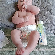 Jameson is registered to the contest to win money with this photo: baby, infant, diaper, bottle, milk, blanket, quilt, hand, foot, face, skin, lying_down, indoors, comfort, cute, child, person, feeding, notebook, relaxing