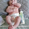 baby, infant, diaper, bottle, milk, blanket, quilt, hand, foot, face, skin, lying_down, indoors, comfort, cute, child, person, feeding, notebook, relaxing