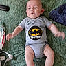 Jameson is registered to the contest to win money with this photo: baby, infant, onesie, batman_logo, lying_down, green_background, baby_wipes, blue_cloth, arm_motion, cute, child, person, soft_lighting, indoor, skin, head, legs, expression, clothing, toddler