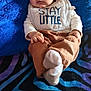 baby, infant, bib, clothing, blanket, blue, brown_pants, white_socks, face, person, cute, portrait, indoor, soft_texture, patterned_background, child, expression, resting, small_hands, warm