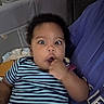 baby, casual, child, comfort, couch, curly_hair, expression, face, finger, hand, holding, home, indoor, infant, person, purple_shirt, seated, striped_shirt, upset, wide_eyes