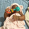 Naela is registered to the contest to win money with this photo: baby, infant, towel, pink, rattle, toy, blanket, lying_down, child, cute, skin, hand, face, hooded_towel, bed, fabric, soft, playful, indoor, comfort
