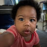 Naela is registered to the contest to win money with this photo: baby, child, infant, portrait, closeup, face, eyes, curious, indoors, pink_clothing, short_sleeves, sitting, reaching, camera, home, furniture, soft_focus, blurred_background, natural_expression, family_photo