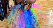 Naela is registered to the contest to win money with this photo: adult, baby, bow, celebration, child, colorful, costume, curly_hair, dress, fashion, indoors, playroom, portrait, rainbow, smiling, snacking, supporting, toddler, tutu, wooden_floor