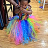 Naela is registered to the contest to win money with this photo: baby, child, toddler, portrait, smiling, rainbow, tutu, dress, costume, colorful, bow, curly_hair, snacking, indoors, wooden_floor, playroom, adult, supporting, fashion, celebration