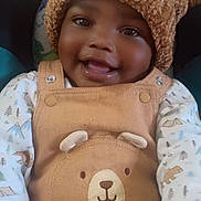 Tyhjzae is registered to the contest to win money with this photo: baby, child, smiling, hat, pom_poms, knit_hat, overalls, bear_design, cute, happy, face, portrait, infant, clothing, patterned_shirt, indoor, closeup, warm_colors, soft_lighting, young