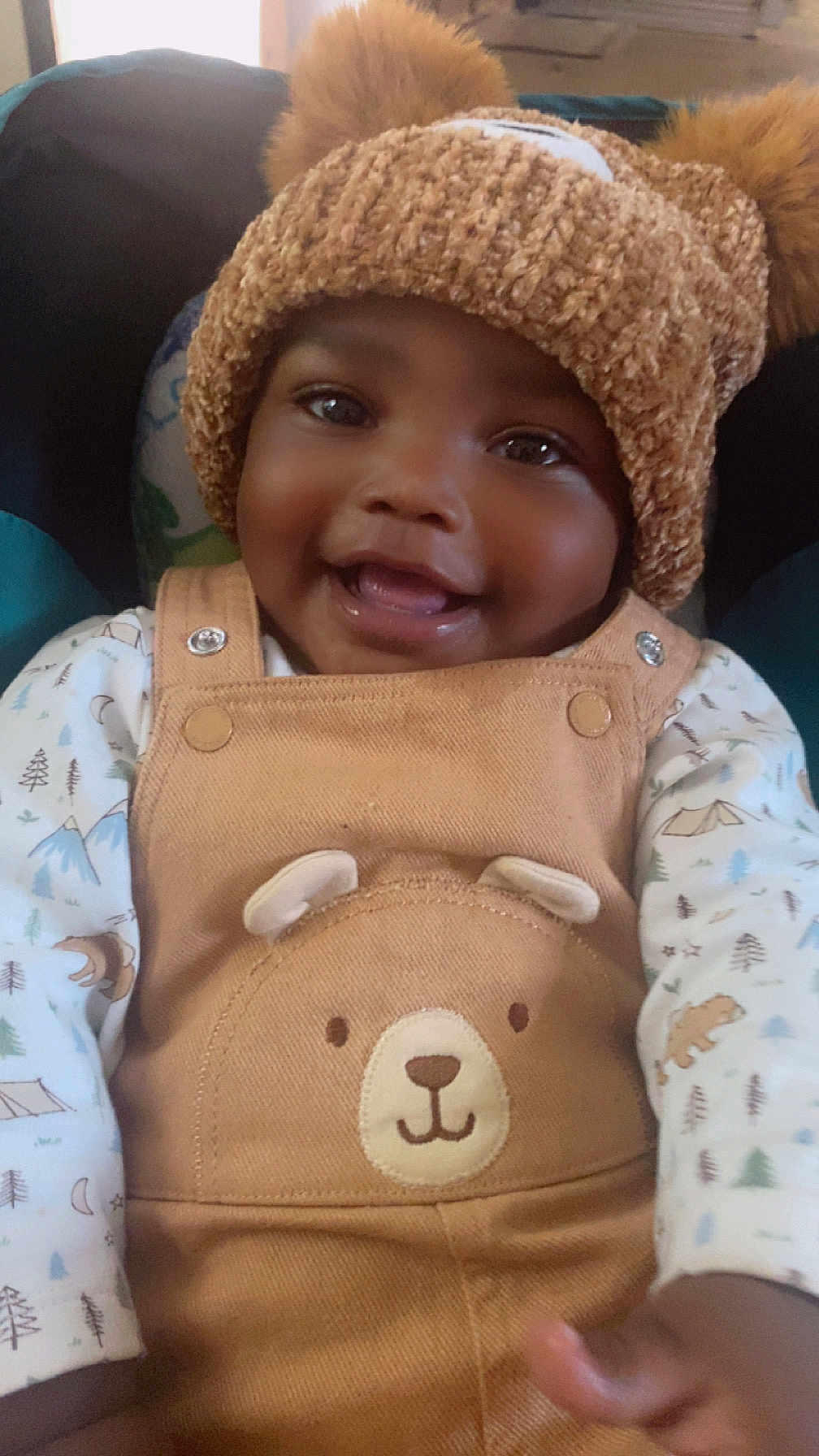 Tyhjzae is registered to the contest to win money with this photo: baby, child, smiling, hat, pom_poms, knit_hat, overalls, bear_design, cute, happy, face, portrait, infant, clothing, patterned_shirt, indoor, closeup, warm_colors, soft_lighting, young