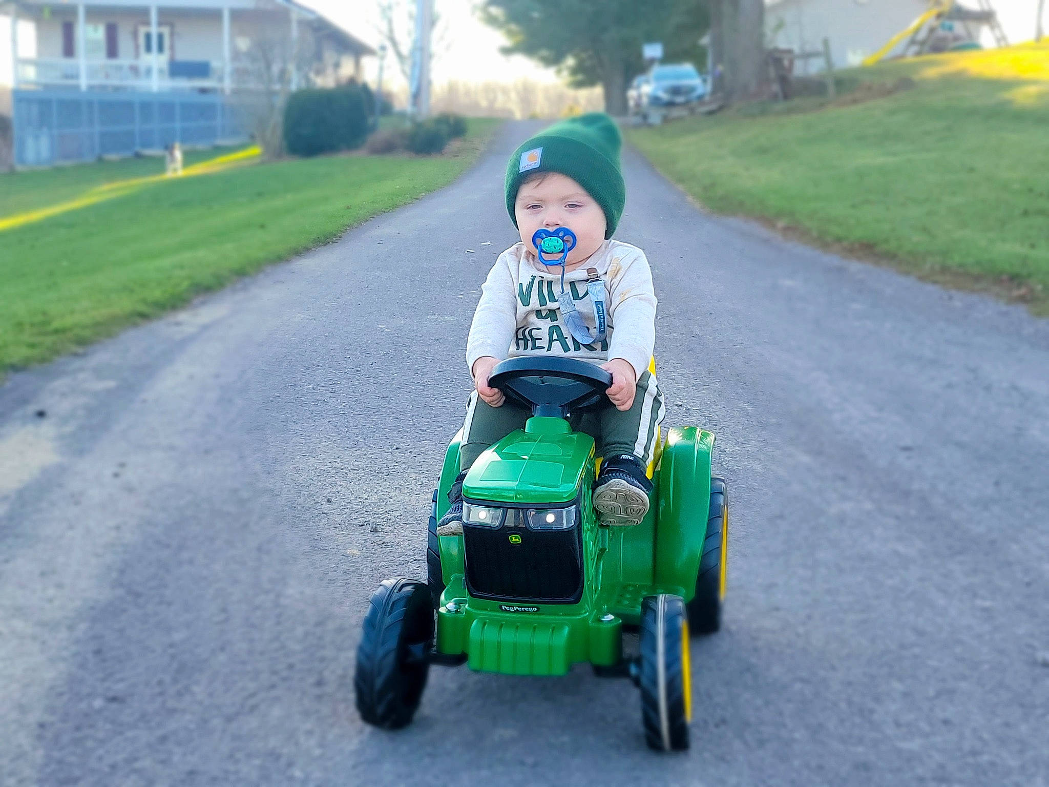 Hudson is registered to the contest to win money with this photo: agricultural_machinery, asphalt, auto_part, automotive_design, automotive_tire, automotive_wheel_system, grass, grassland, headwear, lawn, motor_vehicle, person, plant, riding_toy, road, rolling, tire, toddler, tractor, tree