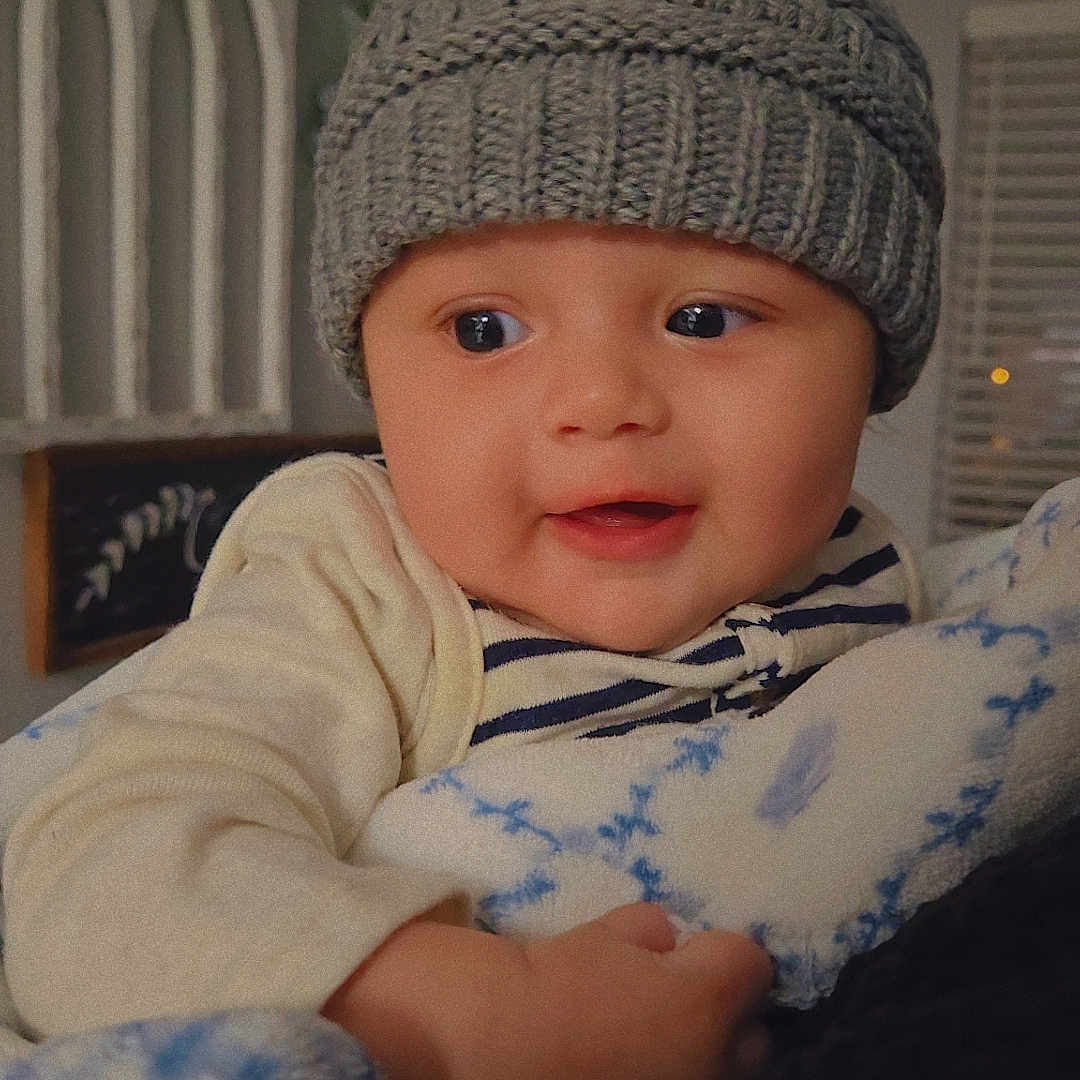 Liam is registered to the contest to win money with this photo: baby, beanie, blackboard, bonnet, cap, clothing, couch, face, furniture, hat, head, knitwear, newborn, person, photography, portrait, sweater