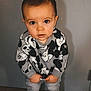toddler, child, mickey_mouse, sweater, standing, curious, indoors, floor, jeans, black_socks, person, portrait, casual_clothing, looking_at_camera, young_child, expression, full_body, wooden_floor, plain_wall, cute
