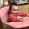 baby, high_chair, pink, smiling, indoor, child, curly_hair, kitchen, snacks, stacked_items, wooden_counter, tableware, person, cute, happy, sitting, clothing, long_sleeves, polka_dots, infant