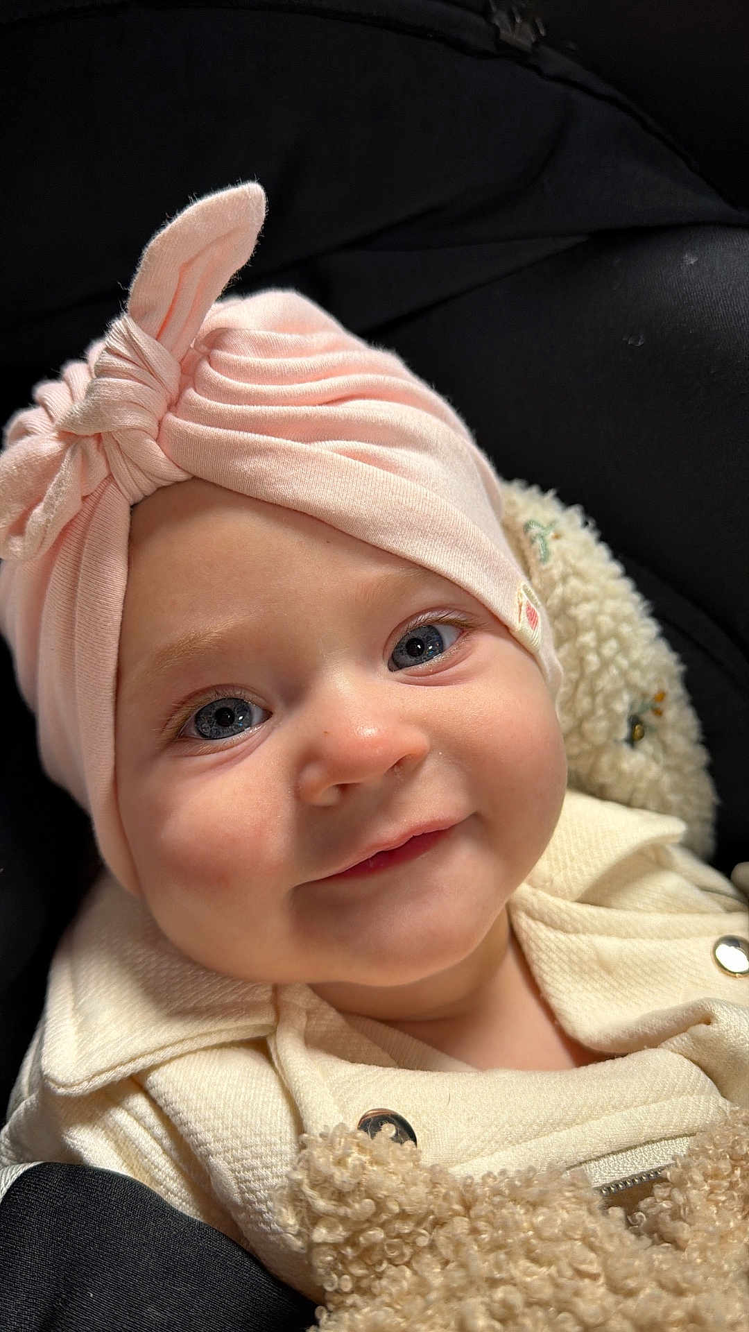 Georgia a rejoint le concours — aidez-le/la à gagner de superbes lots ! baby, infant, portrait, close_up, hat, headwrap, pink_headwrap, blue_eyes, smile, rosy_cheeks, eyelashes, cozy, blanket, jacket, button, fuzzy_texture, car_seat, black_background, soft_lighting, adorable