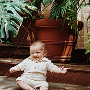 Lorenzo joined the competition — help win amazing prizes! baby, child, smiling, sitting, plants, greenery, terracotta_pot, indoors, concrete_floor, cute, happy, infant, portrait, natural_light, casual_clothing, shorts, shirt, barefoot, toddler, playful