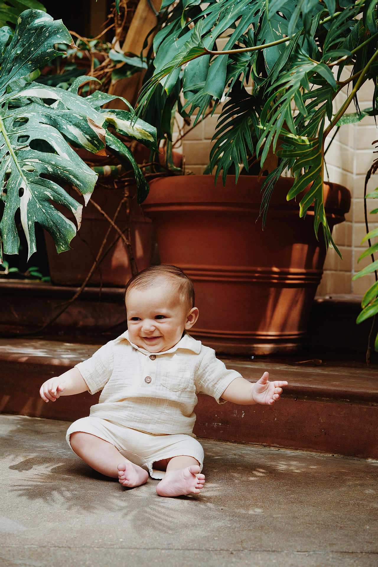Lorenzo joined the competition — help win amazing prizes! baby, child, smiling, sitting, plants, greenery, terracotta_pot, indoors, concrete_floor, cute, happy, infant, portrait, natural_light, casual_clothing, shorts, shirt, barefoot, toddler, playful